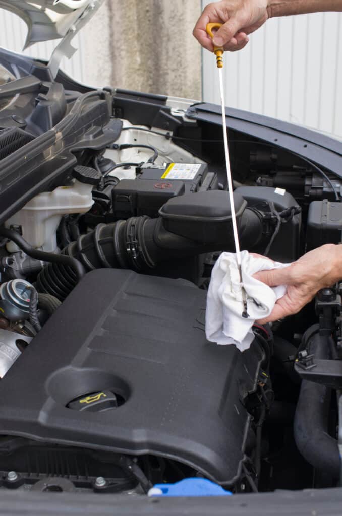 Vérification niveau huile moteur : tutoriel simple Main vérifiant le niveau d'huile moteur avec la jauge jaune, essuyée sur un chiffon blanc, dans un compartiment moteur ouvert.