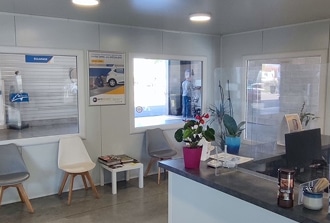 Accueil Atelier Automobile : Attente Confortable et Service Proche Intérieur d'une salle d'attente d'atelier automobile propre, avec chaises modernes, plantes, comptoir et fenêtre donnant sur l'espace de service affichant 'SOLANGA'.