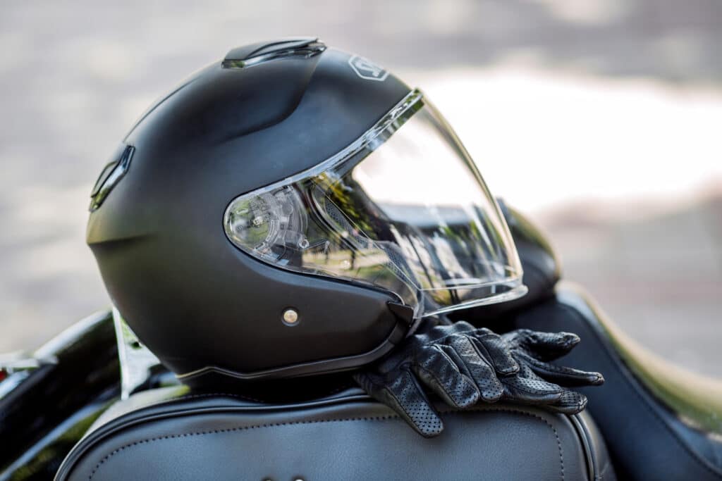 Casque Moto Noir Mat et Gants en Cuir de Protection Casque de moto noir mat et gants en cuir perforé posés sur une selle.
