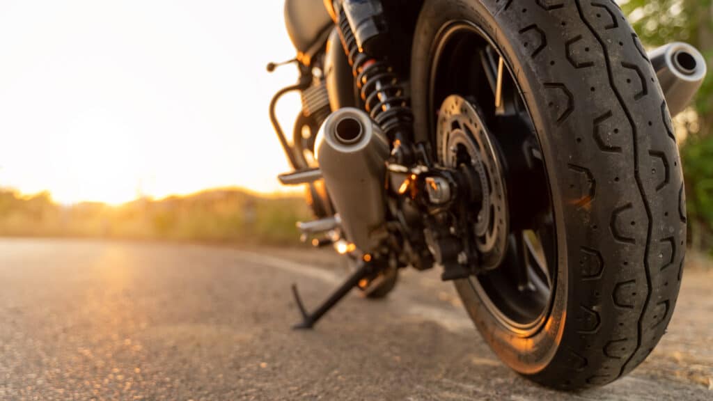 Moto au Coucher du Soleil : Vue Arrière et Échappement Pneu arrière et échappement de moto sur route au coucher du soleil, ambiance dorée.
