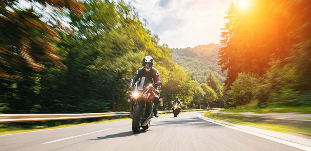 Balade à moto en forêt : vitesse et soleil estival Motard en action sur une route forestière sinueuse et ensoleillée, sensation de vitesse.